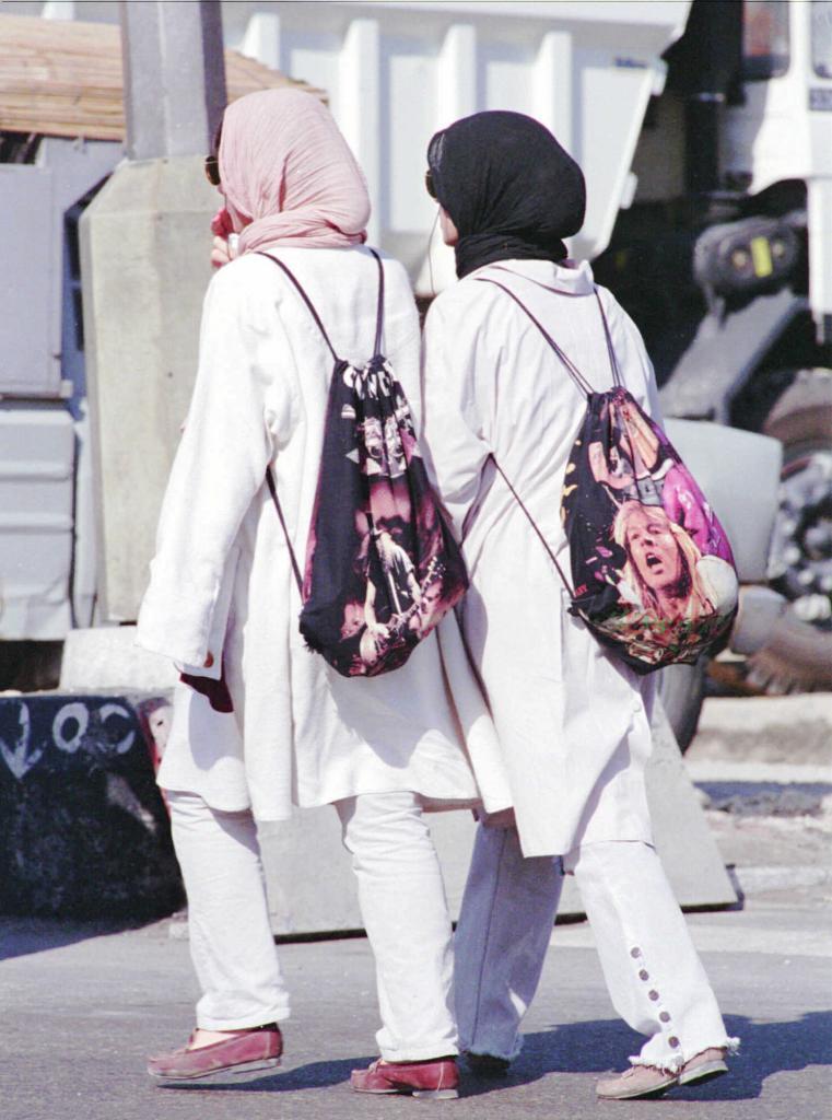 Two young Iranian women, wearing pants and the traditional chador, walk down a street in Tehran.