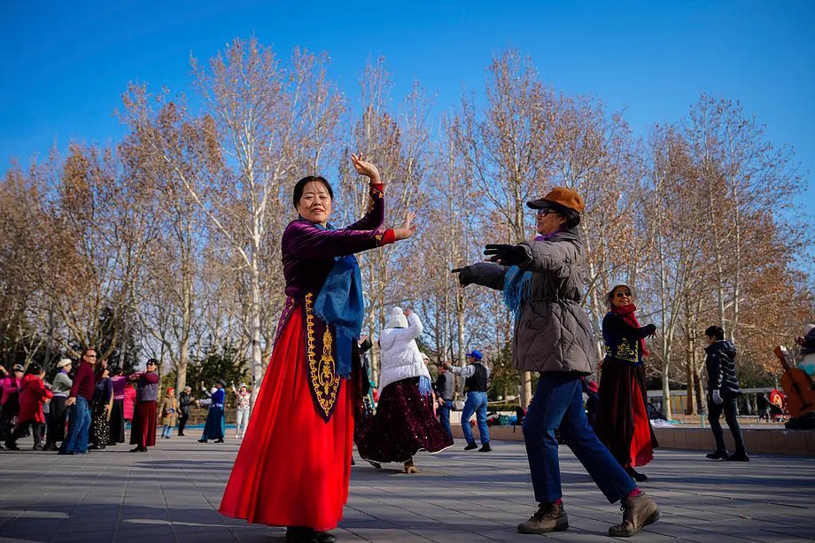 Two women dance in a park in Beijing under a clear sky.