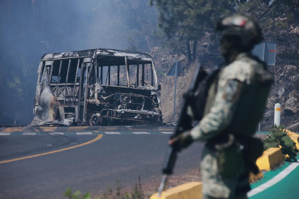 A soldier stands guard by a charred vehicle that was set on fire in Cointzio