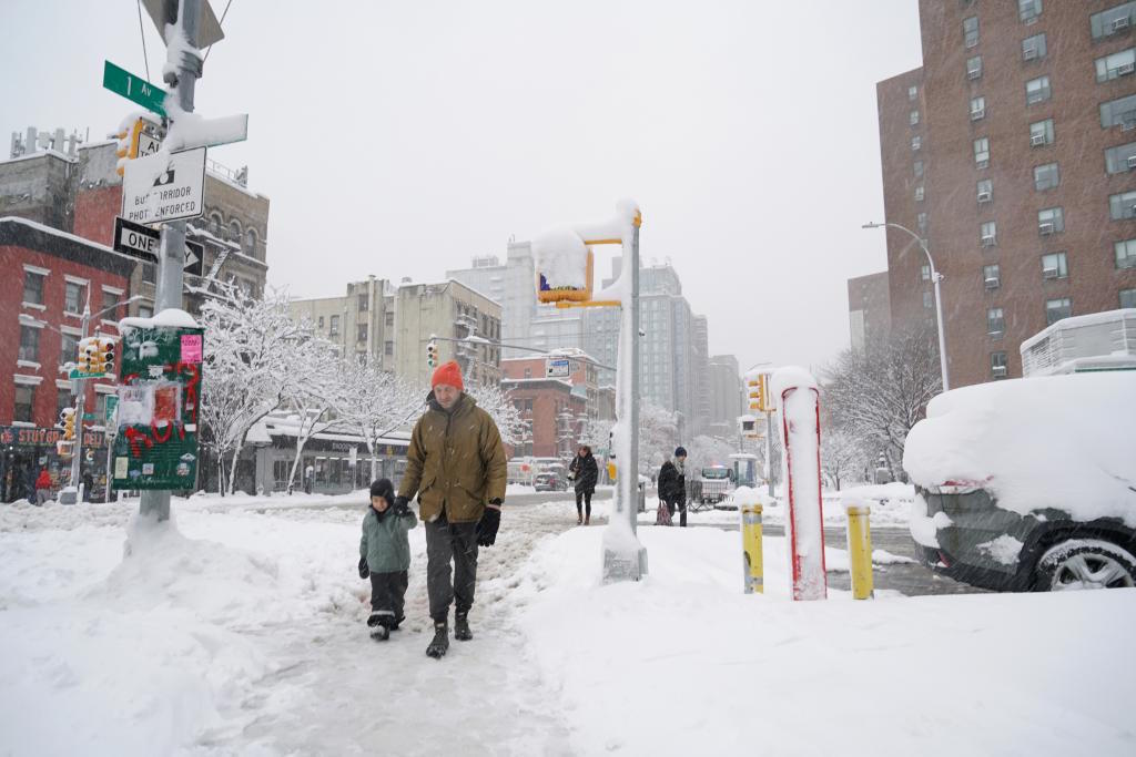 A father walks with his son along First Avenue as the snow falls.
