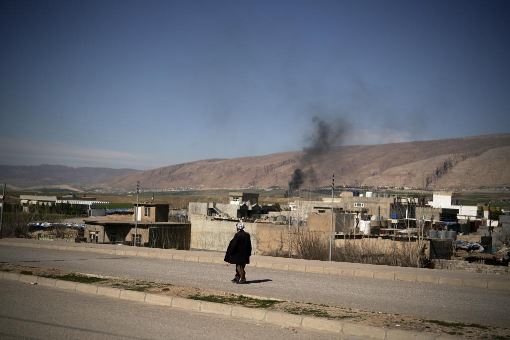 A man walks along a road as smoke rises following attacks early morning in a nearby airbase in Basirma, Iraq,