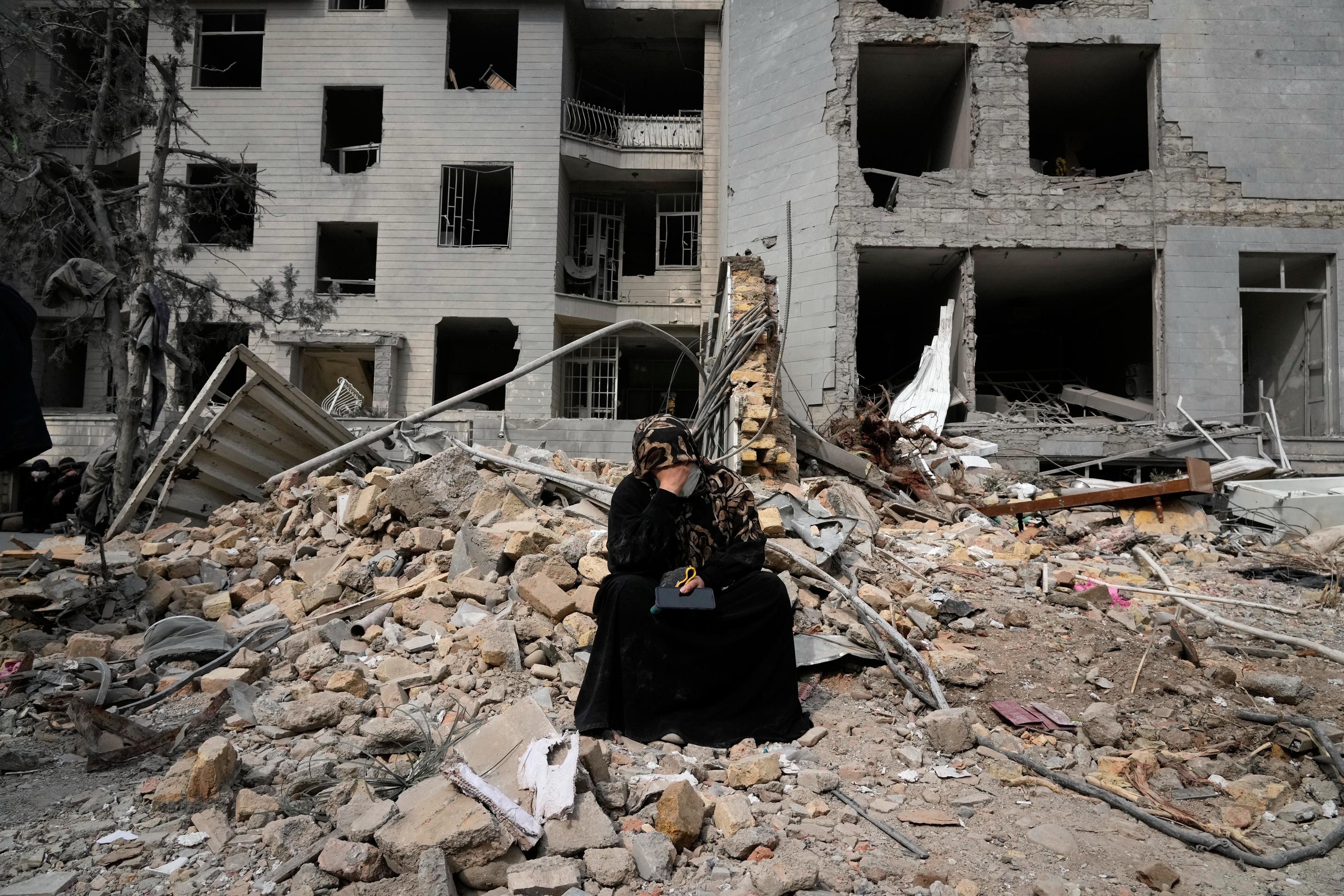 A woman grieves amidst rubble in front of a residential building in Tehran.
