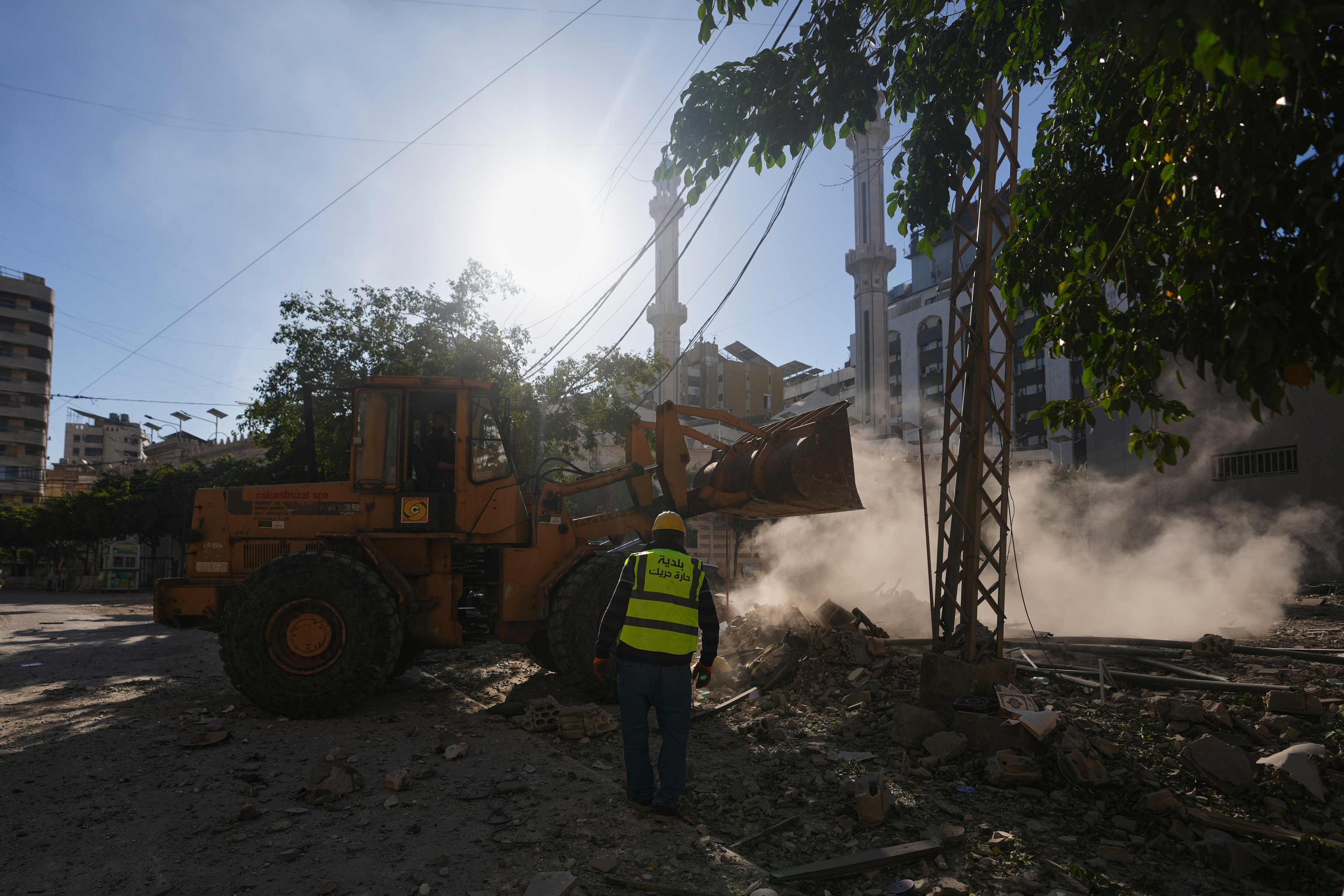 A worker walks near a bulldozer clearing debris from buildings damaged in an Israeli airstrike in Dahiyeh.