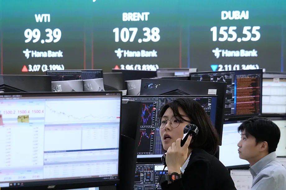 A currency broker works next to a screen displaying international oil prices.