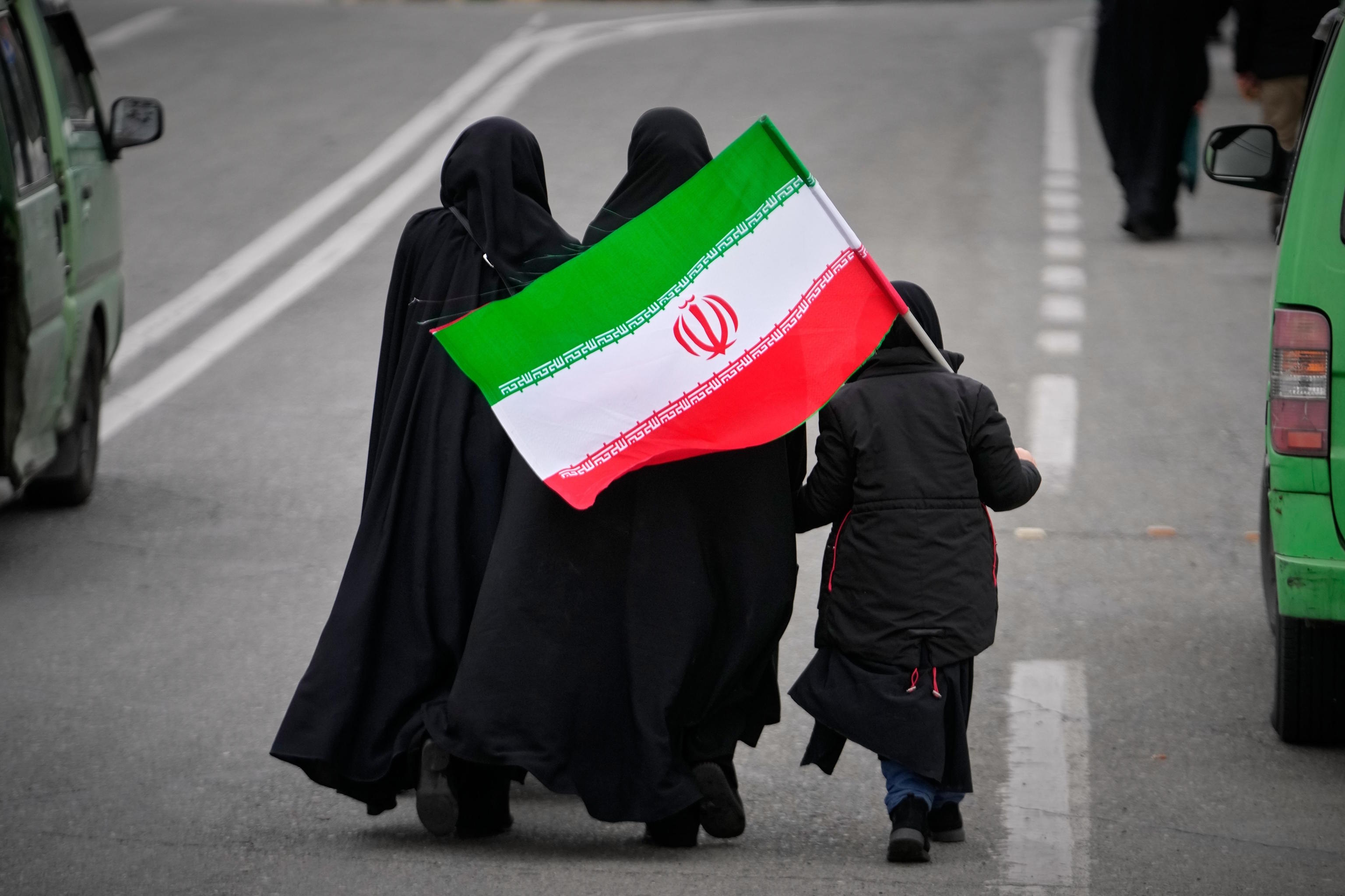 Two women and a minor carrying an Iranian flag walk towards the Grand Mosque.