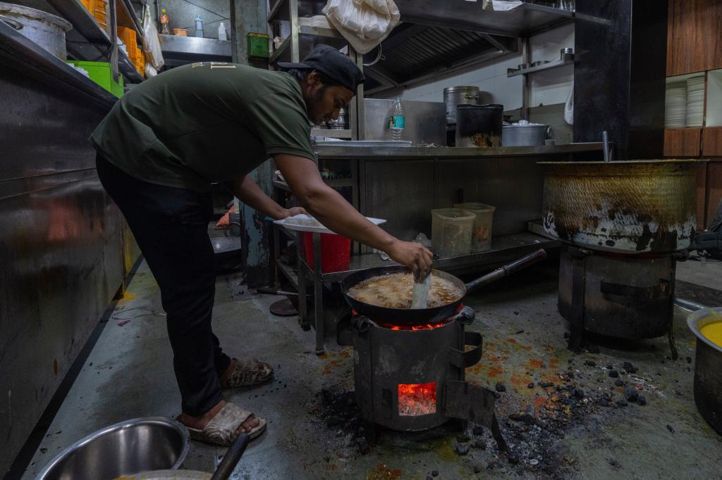 A cook prepares food in a restaurant over a coal stove due to a shortage of liquefied petroleum gas in India.