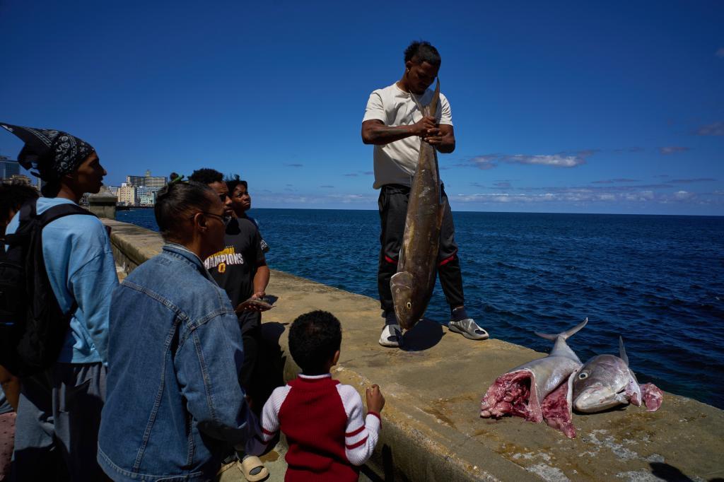 People watch as a man weighs a fish he caught during a blackout in Havana,