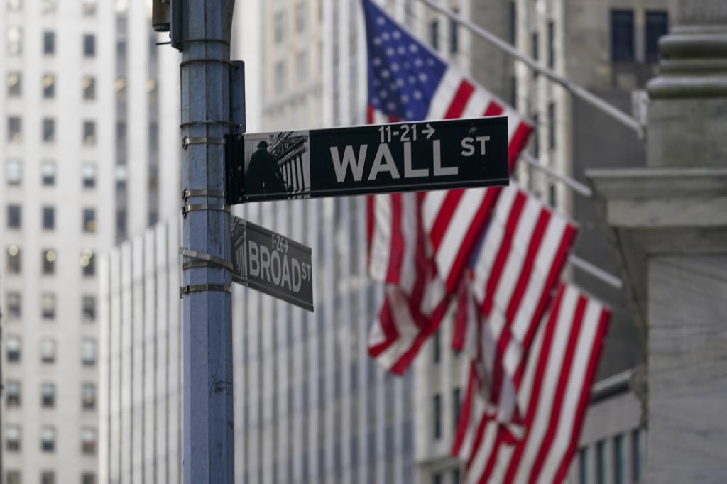 The Wall St. street sign is framed by the American flags flying outside the New York Stock exchange
