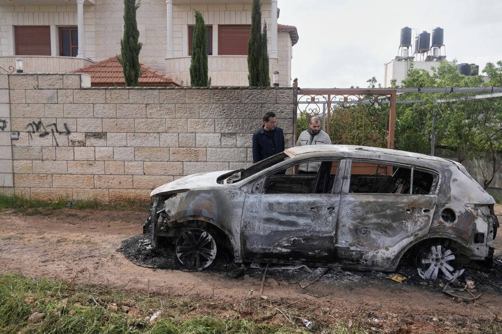 A Palestinian man inspects a torched vehicle next to a Hebrew graffiti on the sidewall that reads "revenge,"