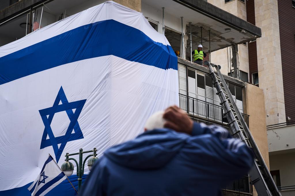 Municipal workers hang a large Israeli flag on a residential building
