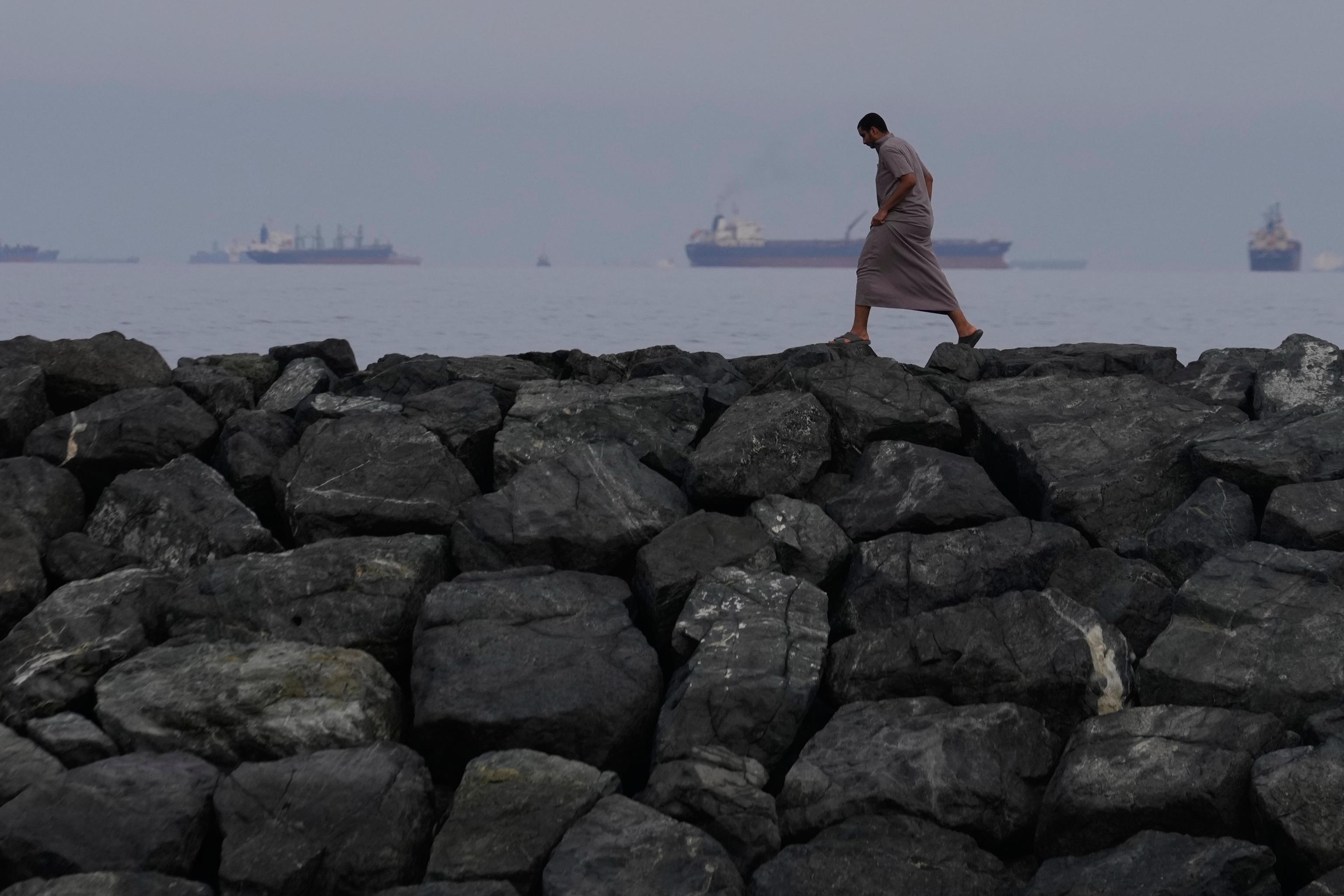 A man walks along the shore as oil tankers and cargo ships line up in the Strait of Hormuz.