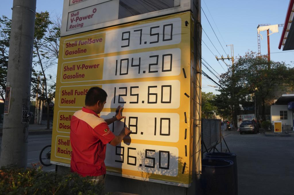 A worker uses black tape to adjust the prices of their sign at a gasoline station as oil prices continue to rise