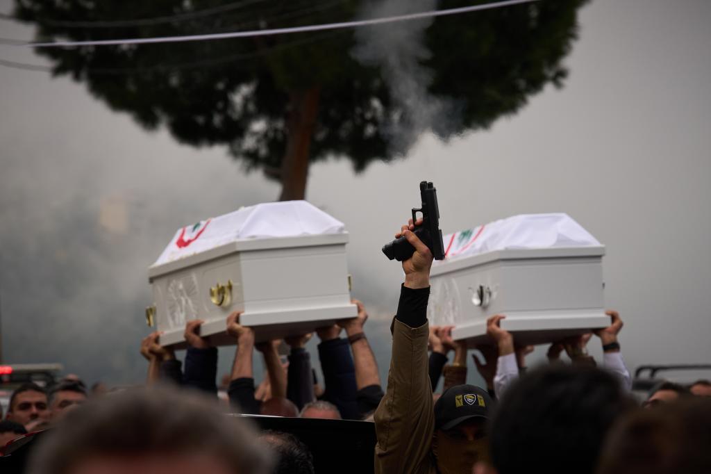 A gunman fires his gun as men carry the coffins with the remains of Pierre Mouawad, an official with the anti-Hezbollah Lebanese Forces party,