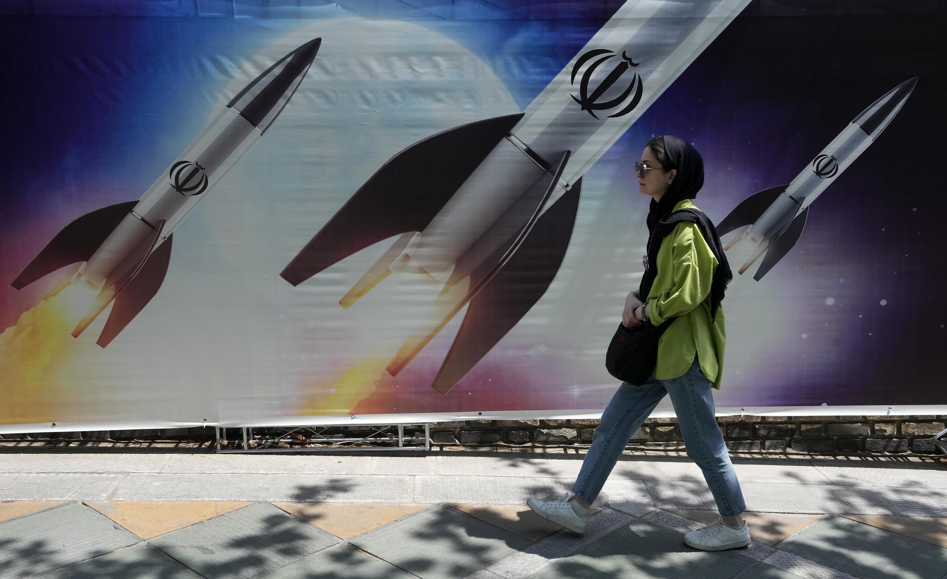 A woman walks past a banner showing missiles being launched, in Tehran.
