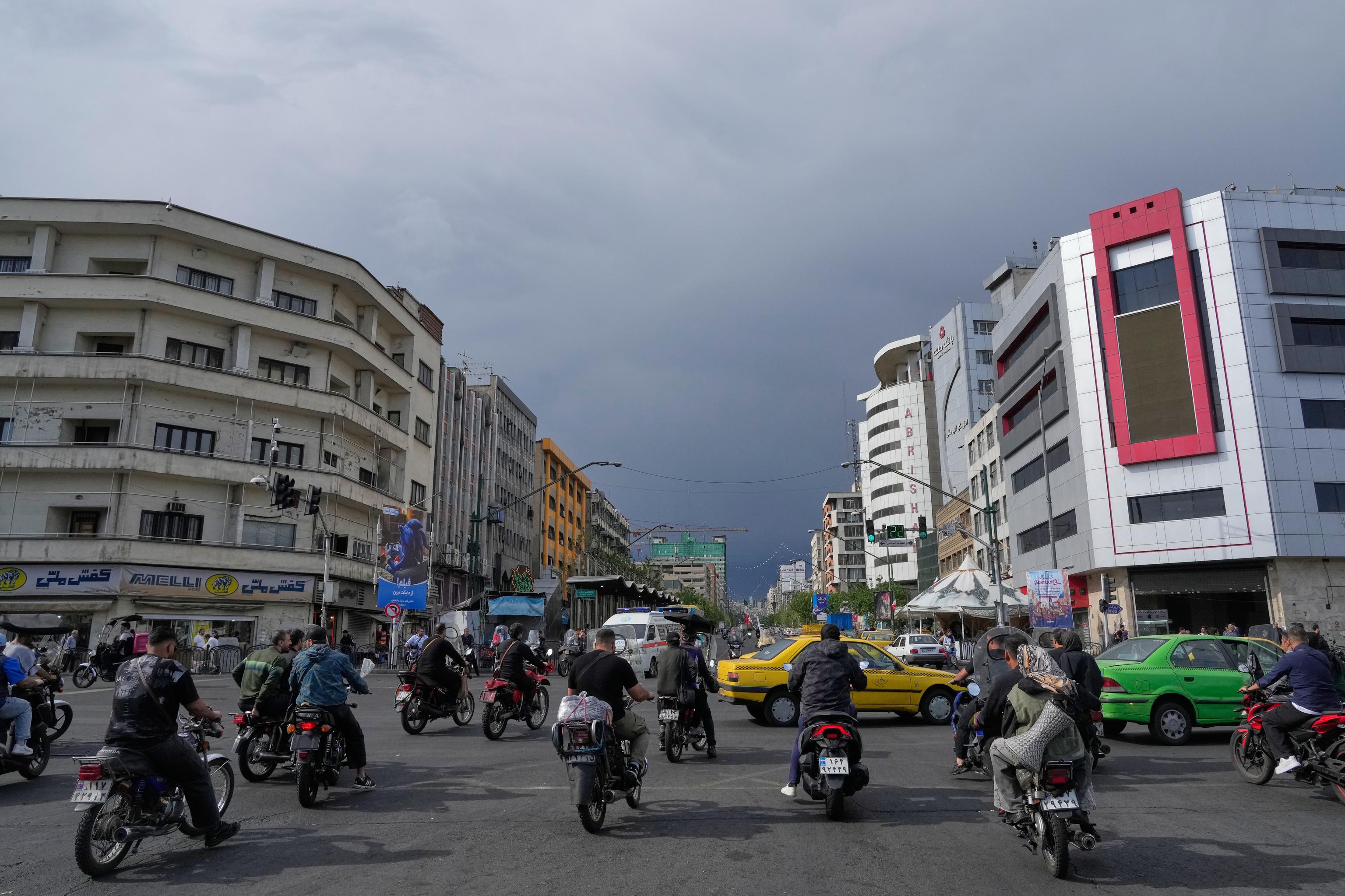 Motorbikes and cars pass through an intersection in downtown Tehran.
