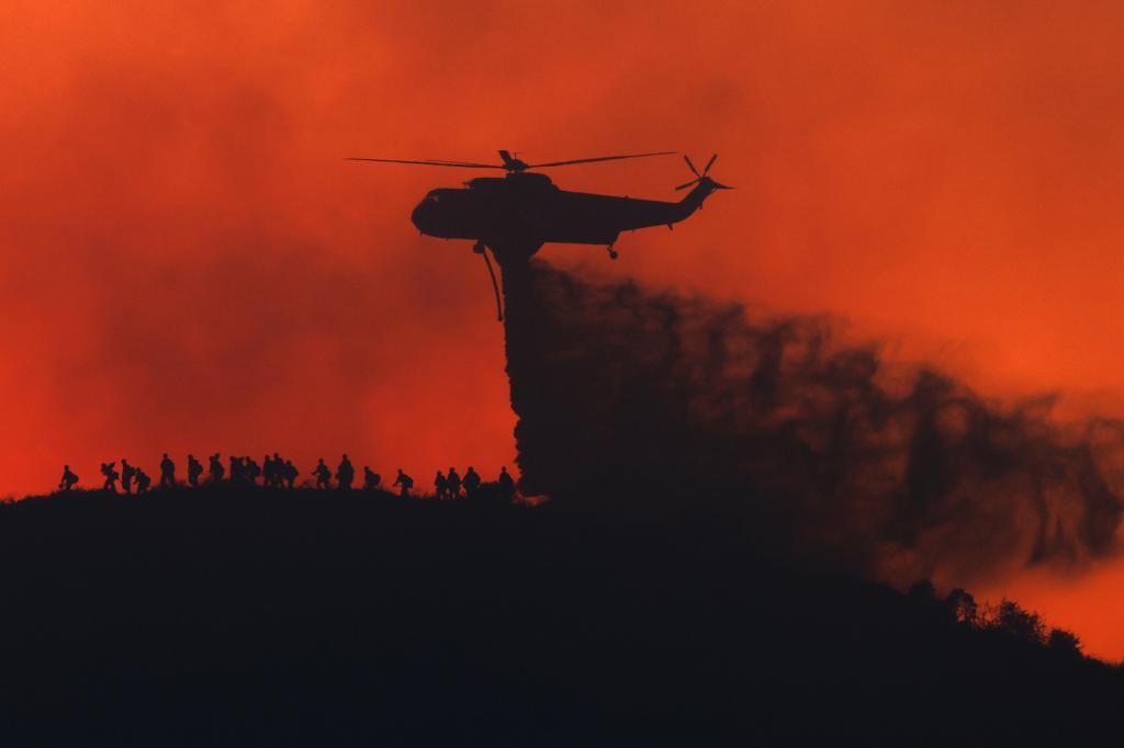 A water tanker drops water while firefighters walk below