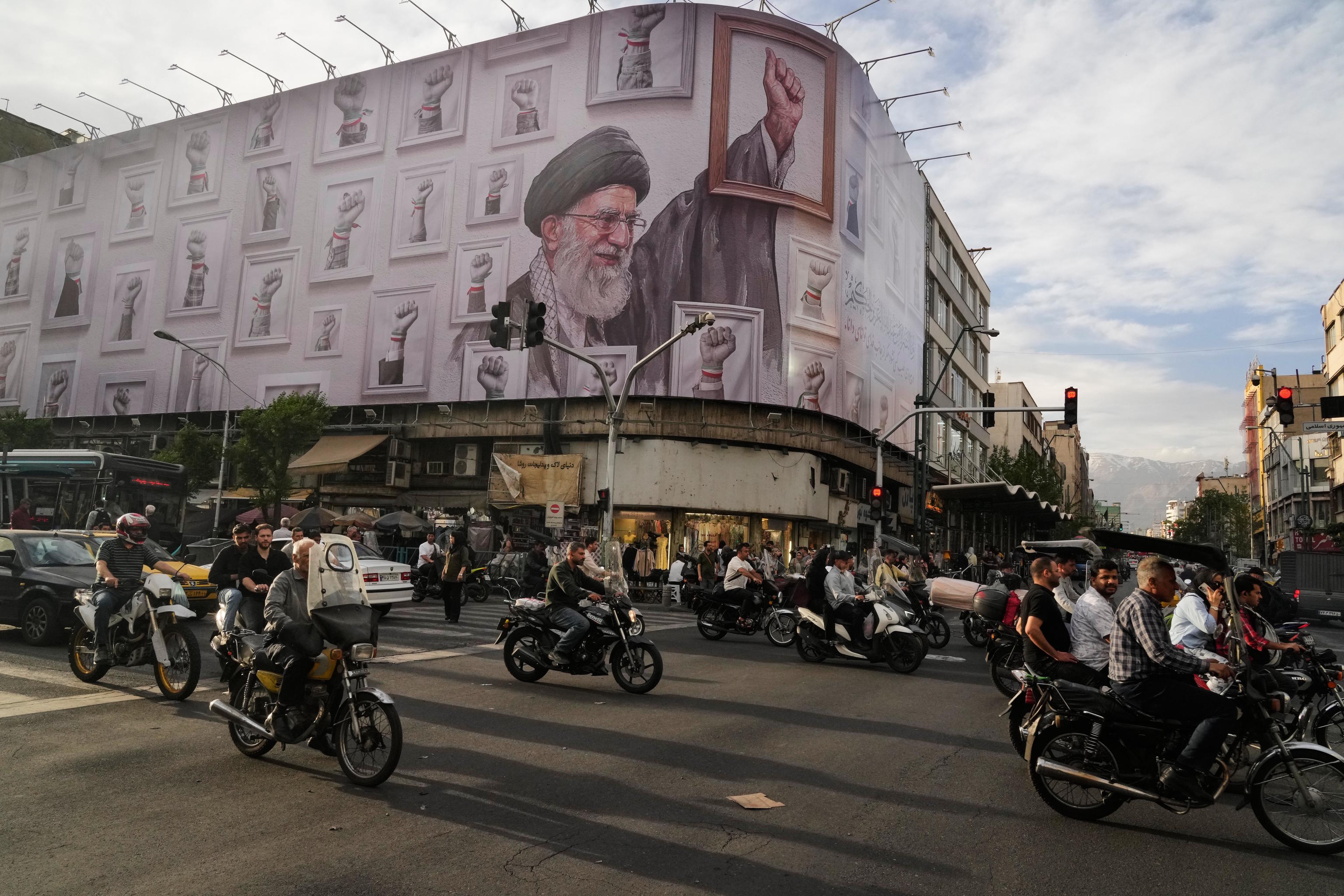 Motorbikes drive past a billboard showing the late Iranian Supreme Leader Ayatollah Ali Khamenei.