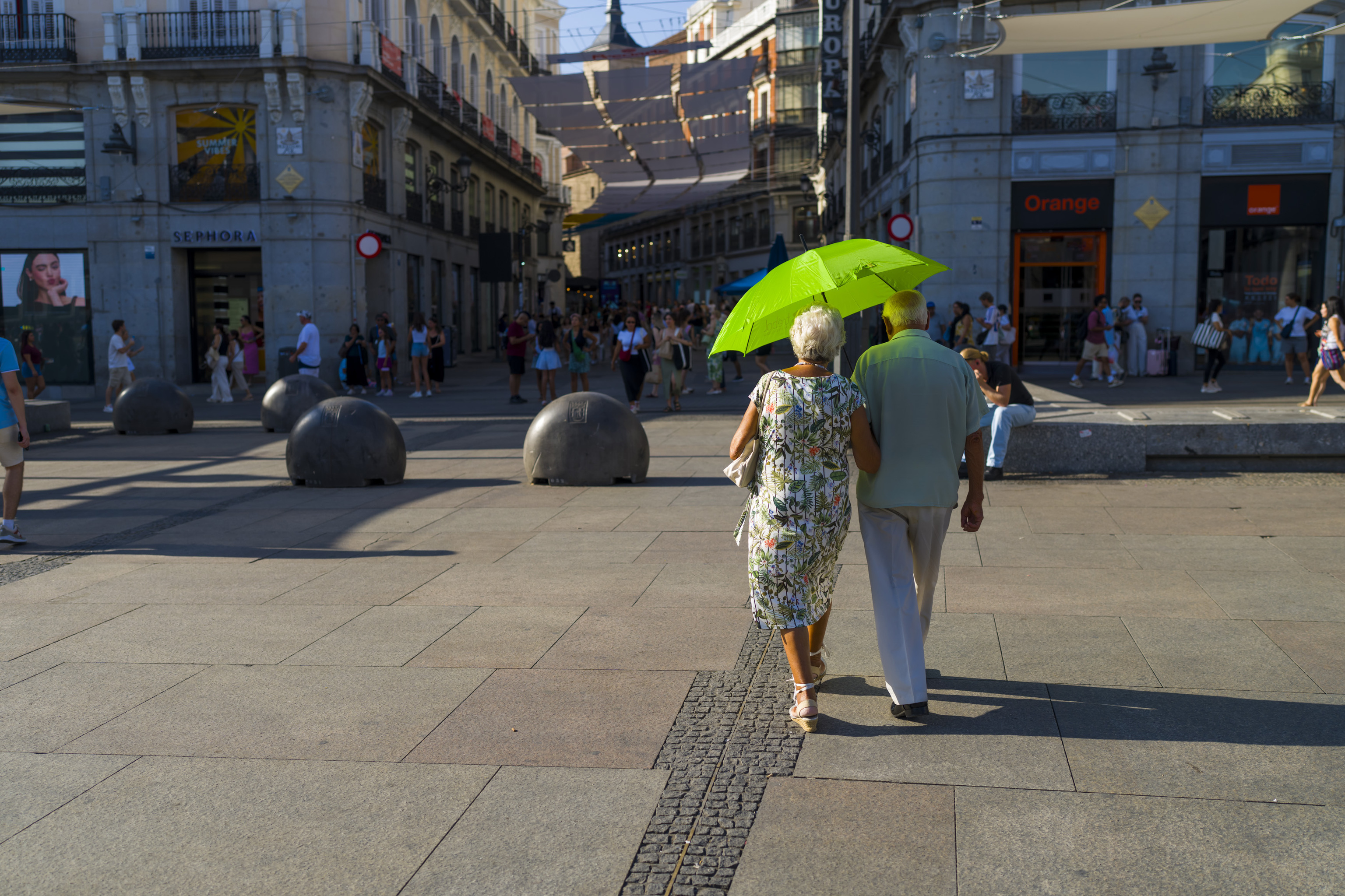 Two elderly people shelter from the sun under an umbrella.