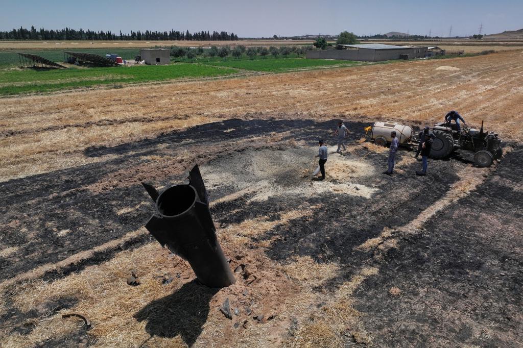 Farmers spray water in a burned agricultural field next to a projectile near the town of Najha