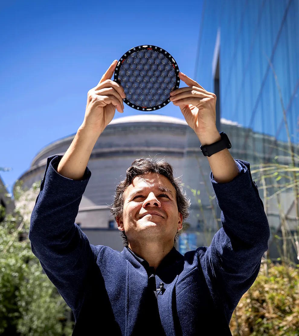 The scientist holds a plastic simulator of the magic angle of graphene, with the MIT dome in the background.