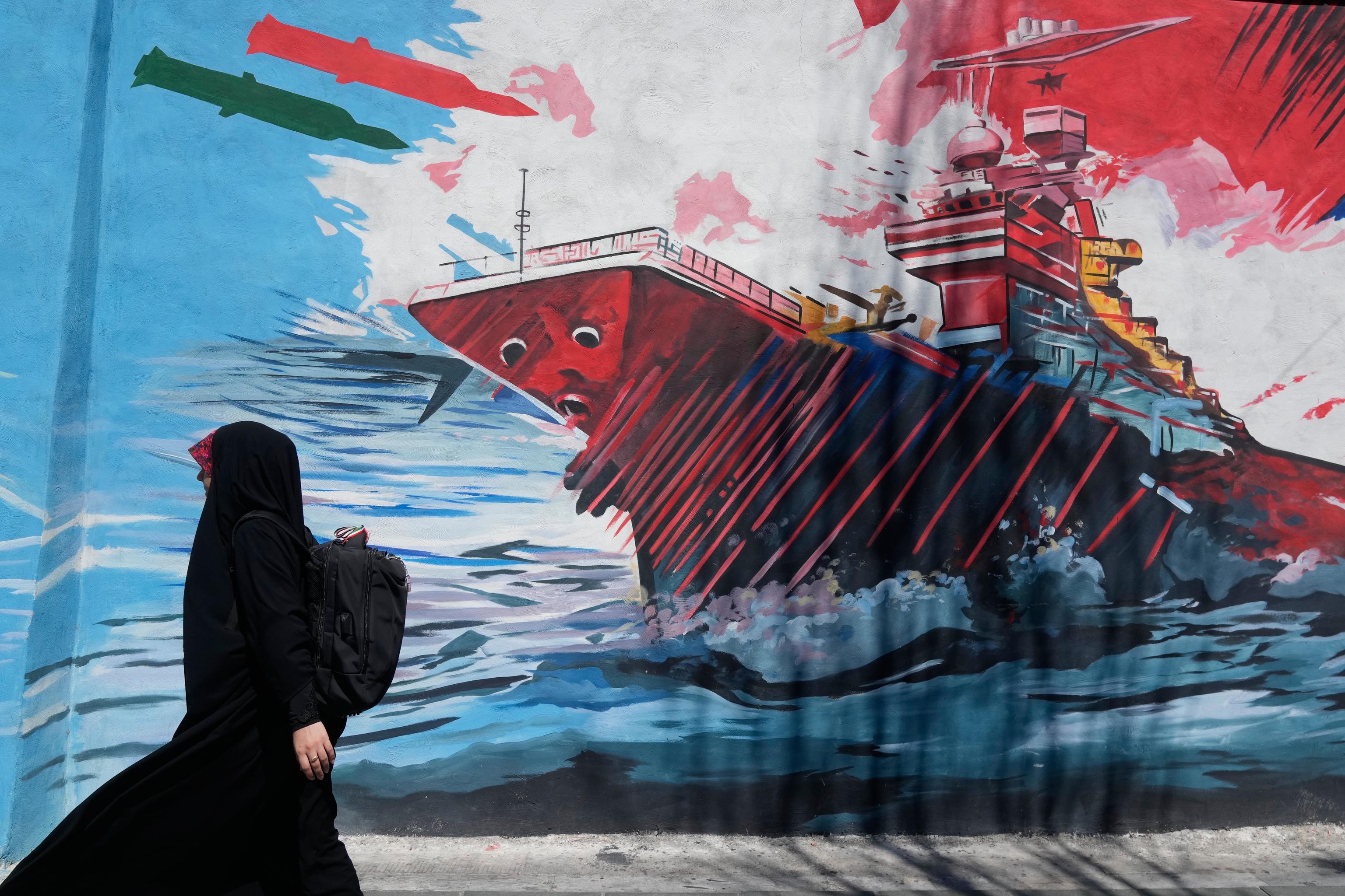 A woman walks past a mural in downtown Tehran depicting a US aircraft carrier under attack.