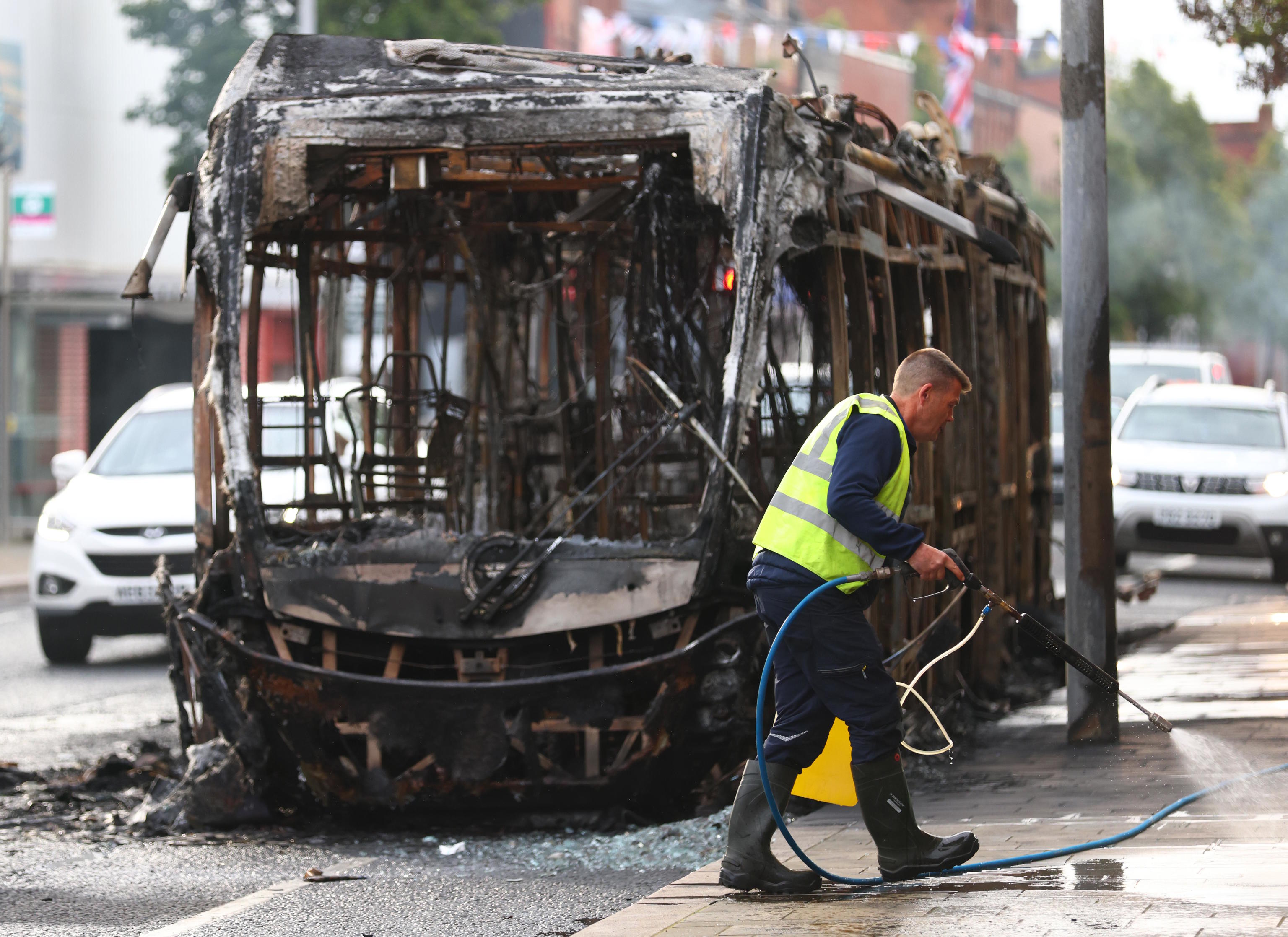 A worker clear up the debris in front of a burnt out bus.