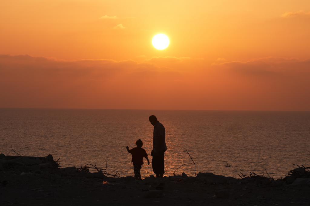 A Palestinian man and his daughter walk along the beach at sunset in Gaza City