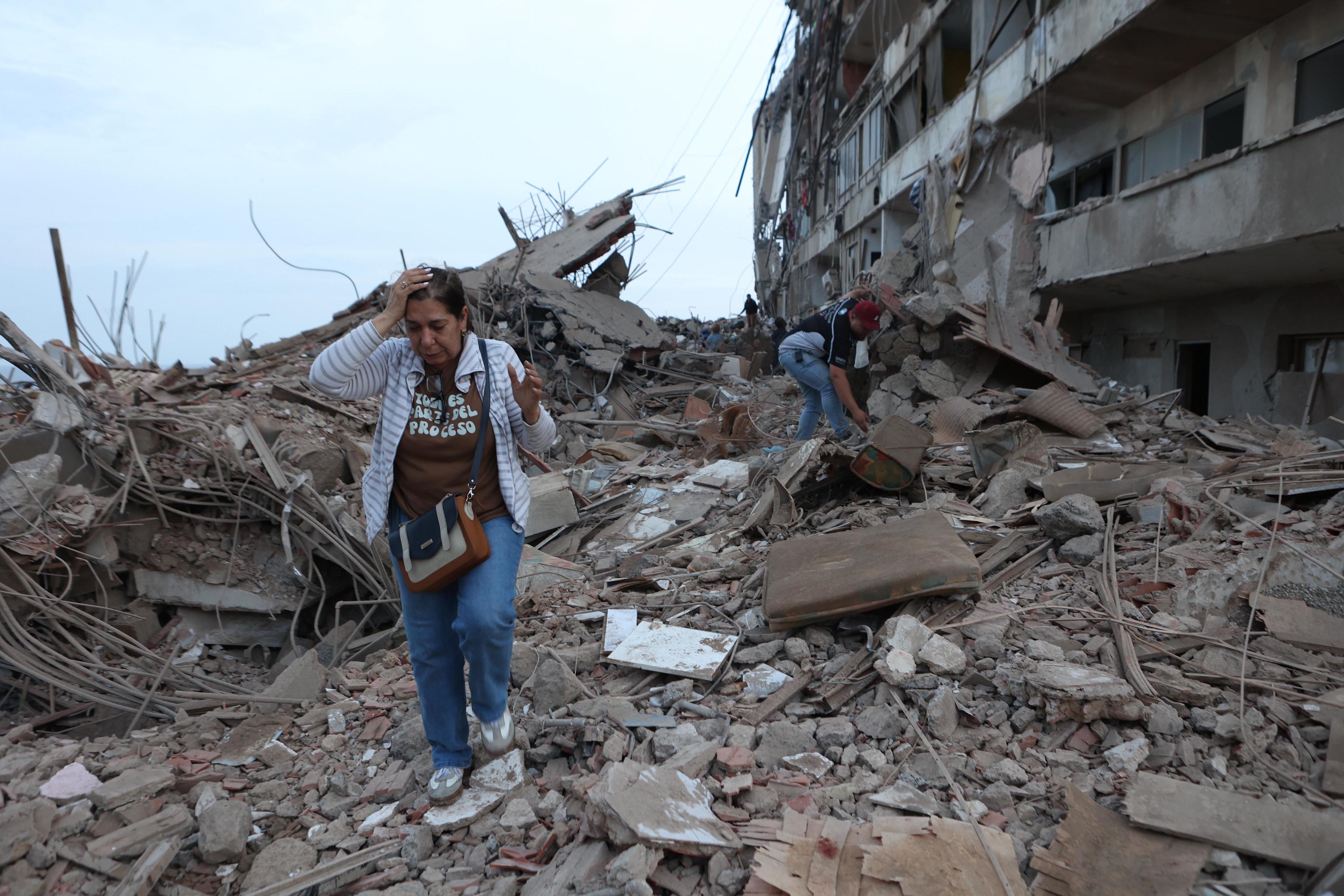 Two women walk among the rubble of damaged buildings.