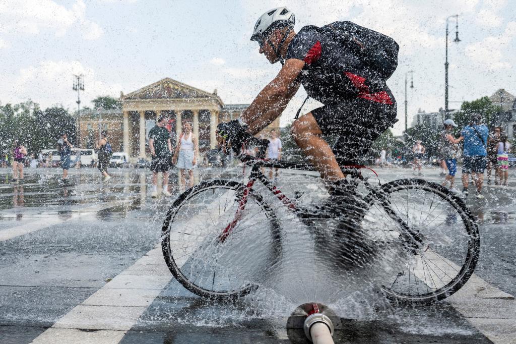 A cyclist rides in front of a police water cannon hose spraying a cooling mist over passersby in Heroes' Square during a heatwave in Budapest