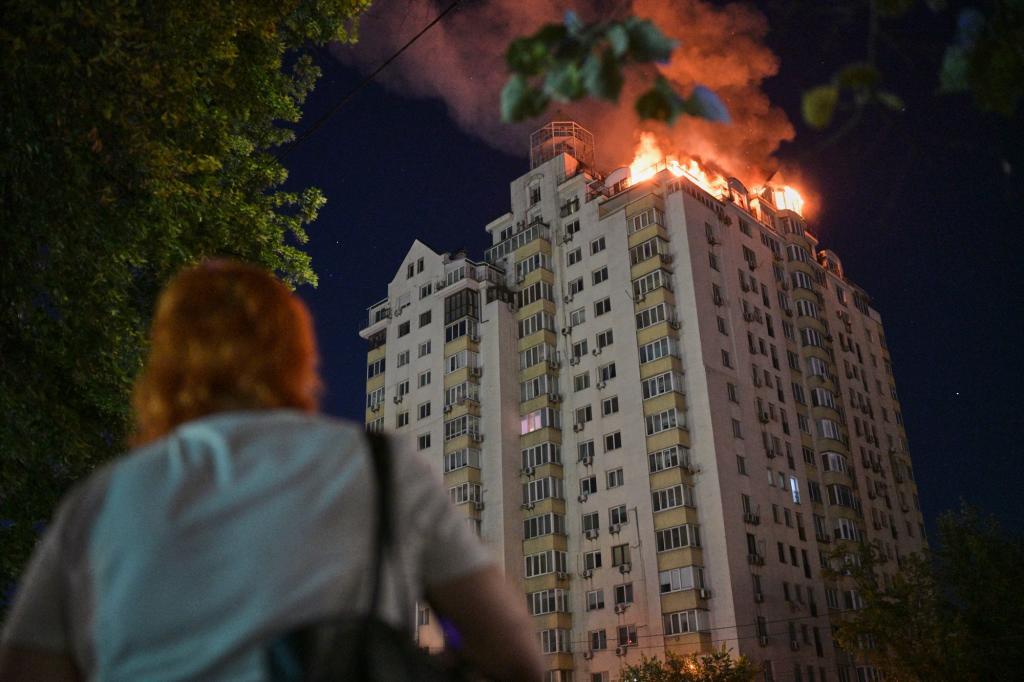 A woman looks at an apartment building burning after a Russian missile attack in Kyiv