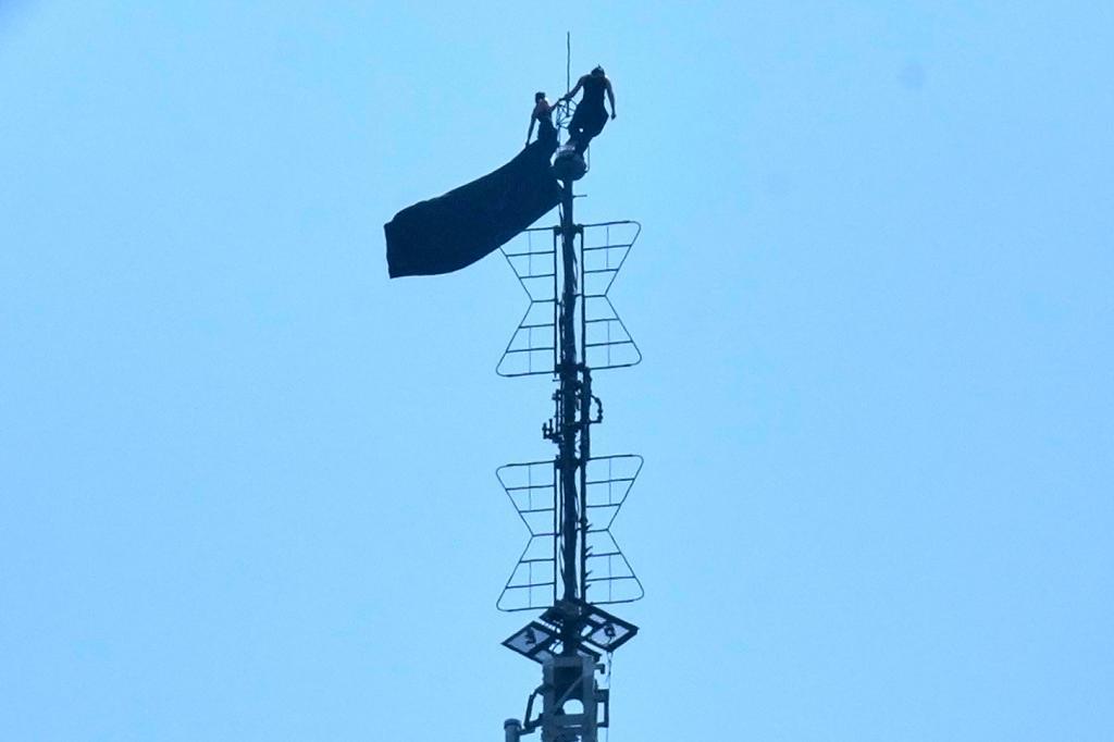 Two people stand on the tip of the antenna of the Empire State Building