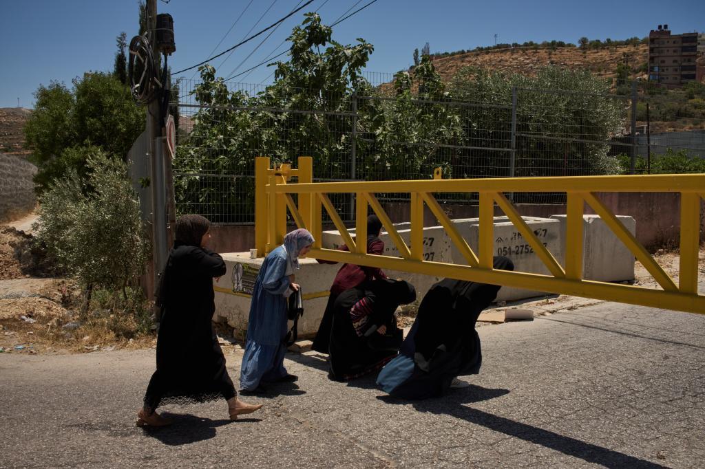 Palestinian women bend down to cross a closed gate after the Israeli army imposed a closure on the entrances of the West Bank