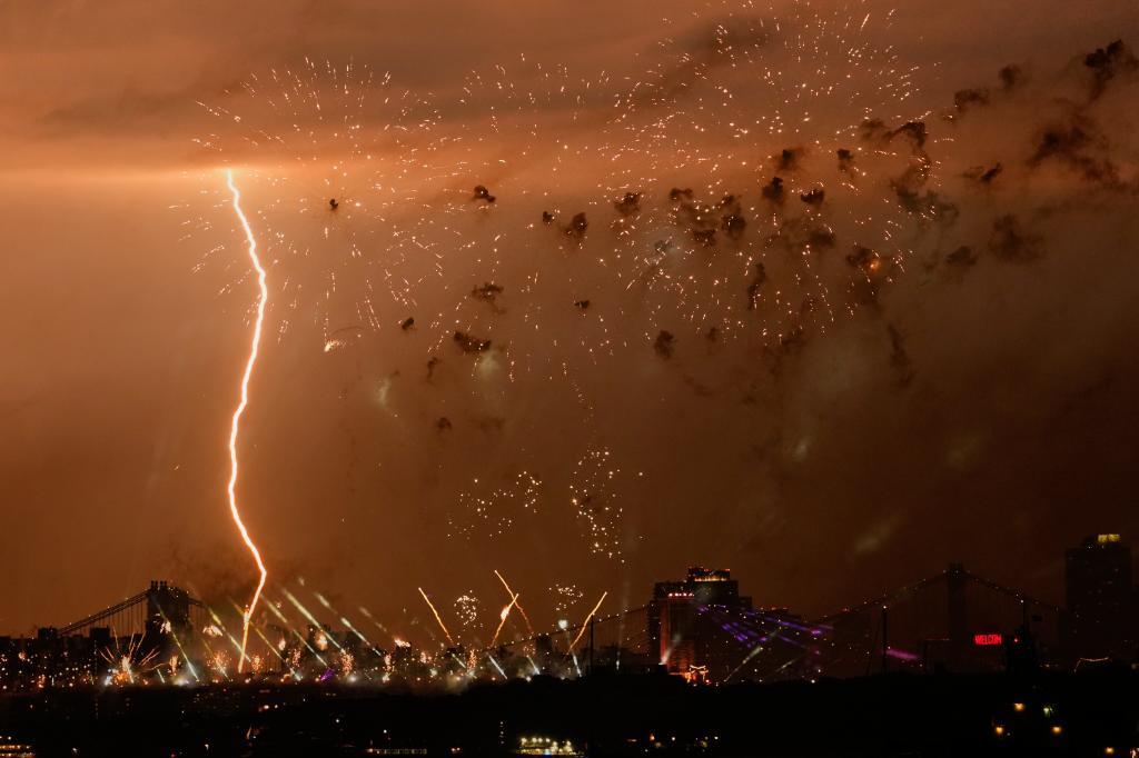A bolt of lightning strikes as fireworks are set off of the Brooklyn Bridge