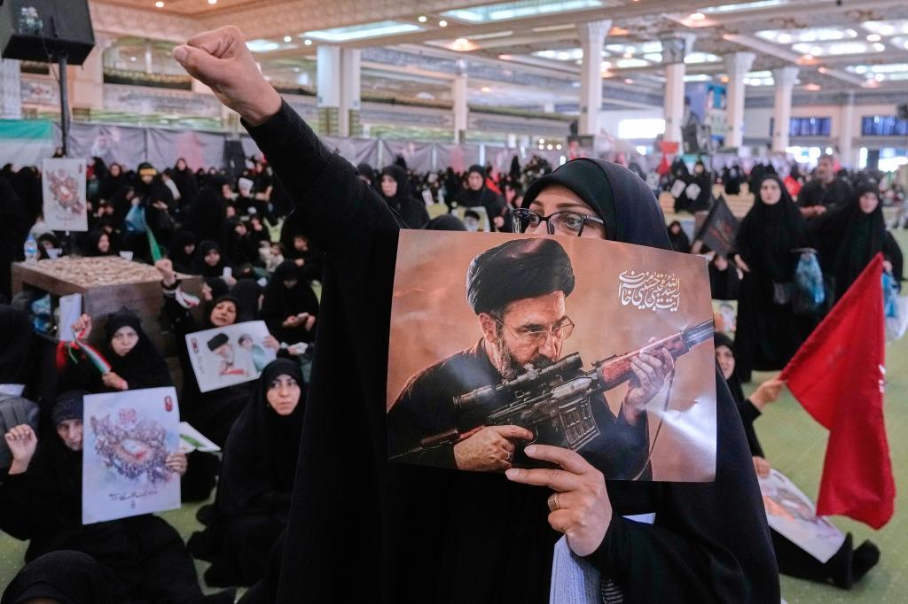 A mourner chants slogan as she holds a poster with graphic depicting Iran's Supreme Leader Ayatollah Mojtaba Khamenei