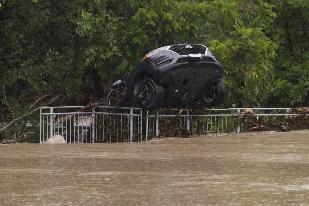 A flood-damaged car hangs from a fence.