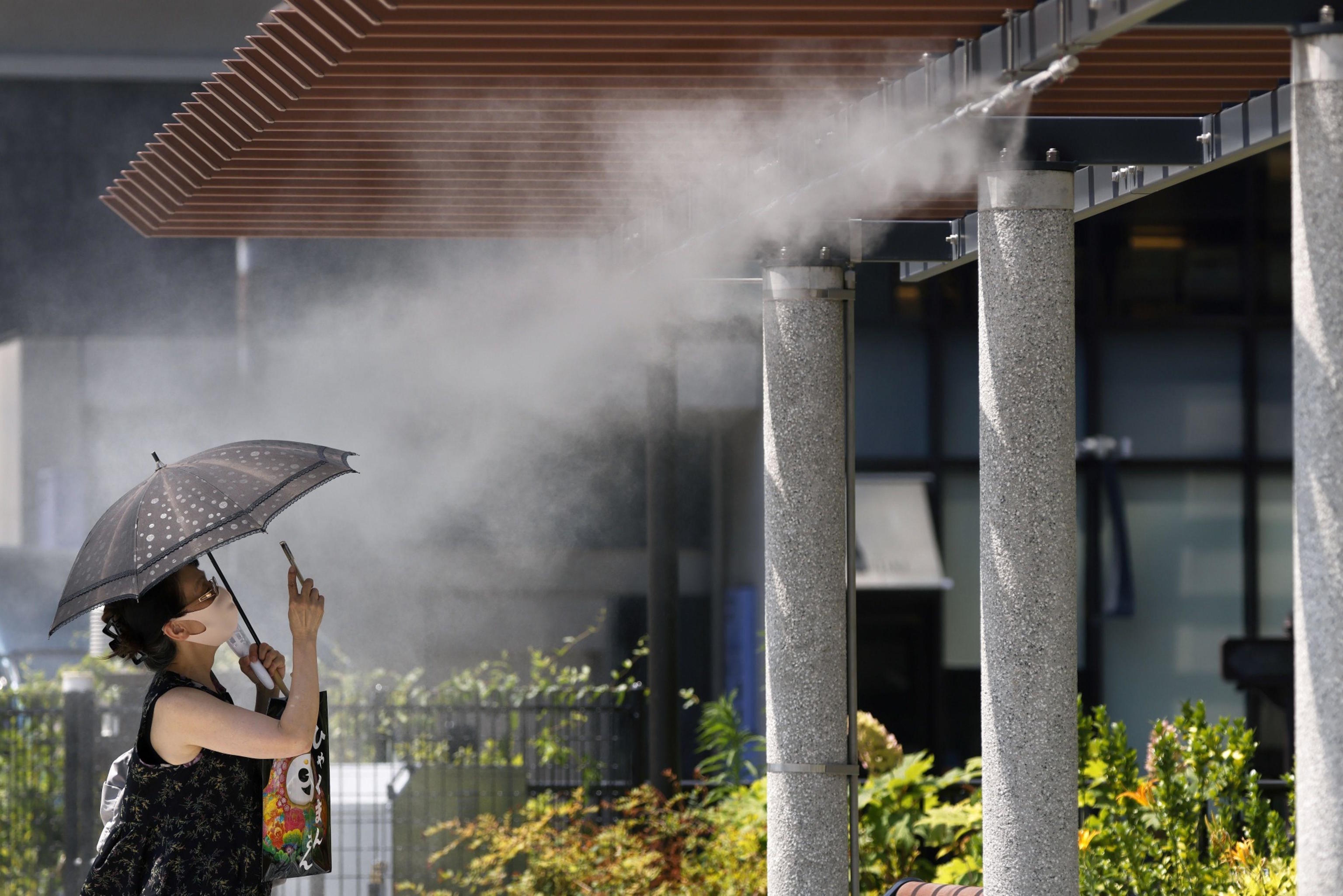 A pedestrian under a cooling mist spray in the Ginza district of Tokyo, Japan.
