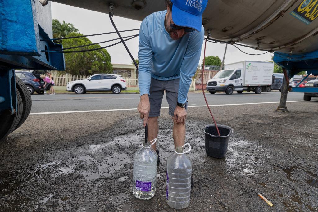 A man fills water jugs from a tanker truck amid drought-driven water rationing, in the Cupey sector of San Juan