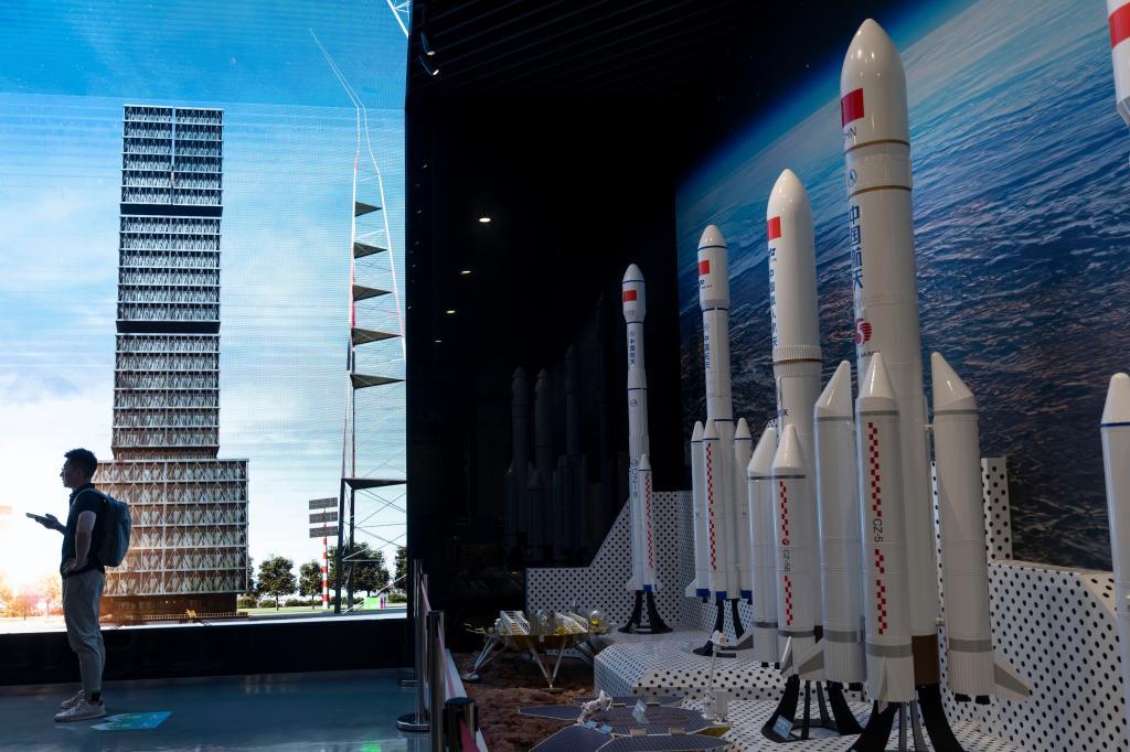 A man is silhouetted near an image of the launch platform and models of space rockets displayed in Haikou in southern China's Hainan
