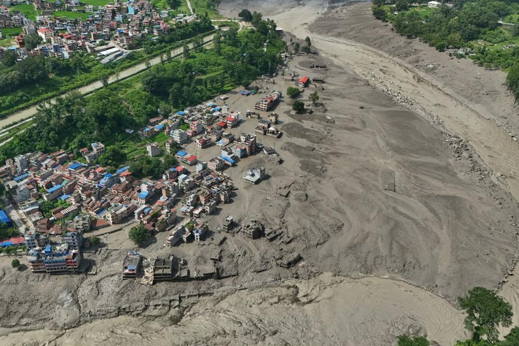 Damaged houses stand precariously near the swollen, debris-choked banks of the Trishuli River
