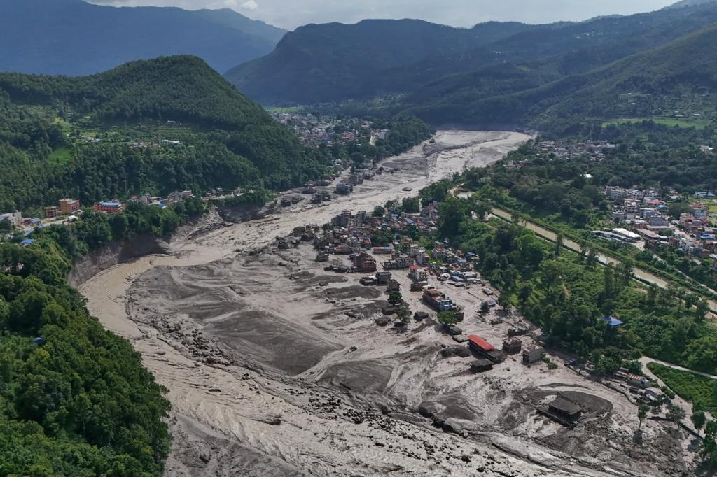 Damaged houses stand precariously near the swollen, debris-choked banks of the Trishuli River