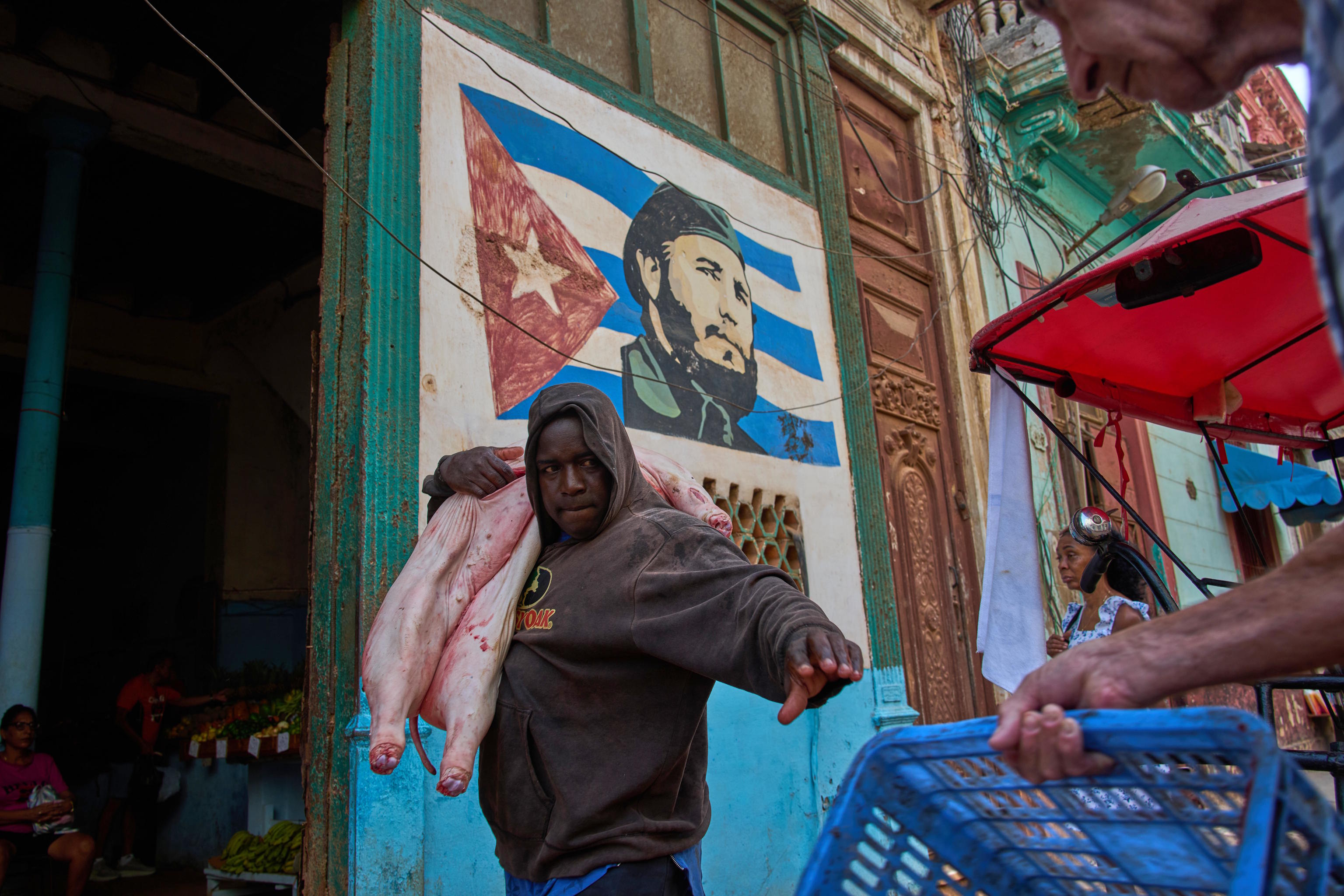 A man carries a pig at the entrance of a market, decorated with a mural of Fidel Castro, in Havana, Cuba.