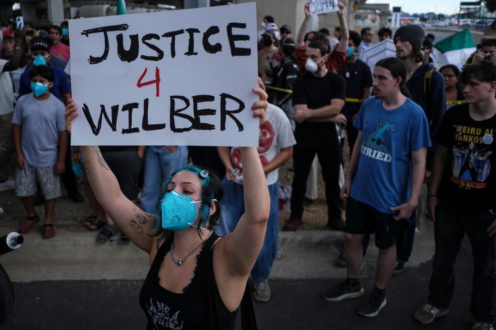 People speak during a demonstration where a man was shot in his vehicle by an ICE officer