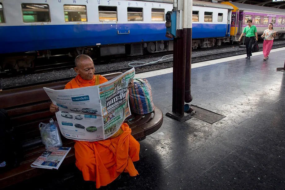 A Thai Buddhist monk reads a newspaper at a train station in Bangkok, Thailand.