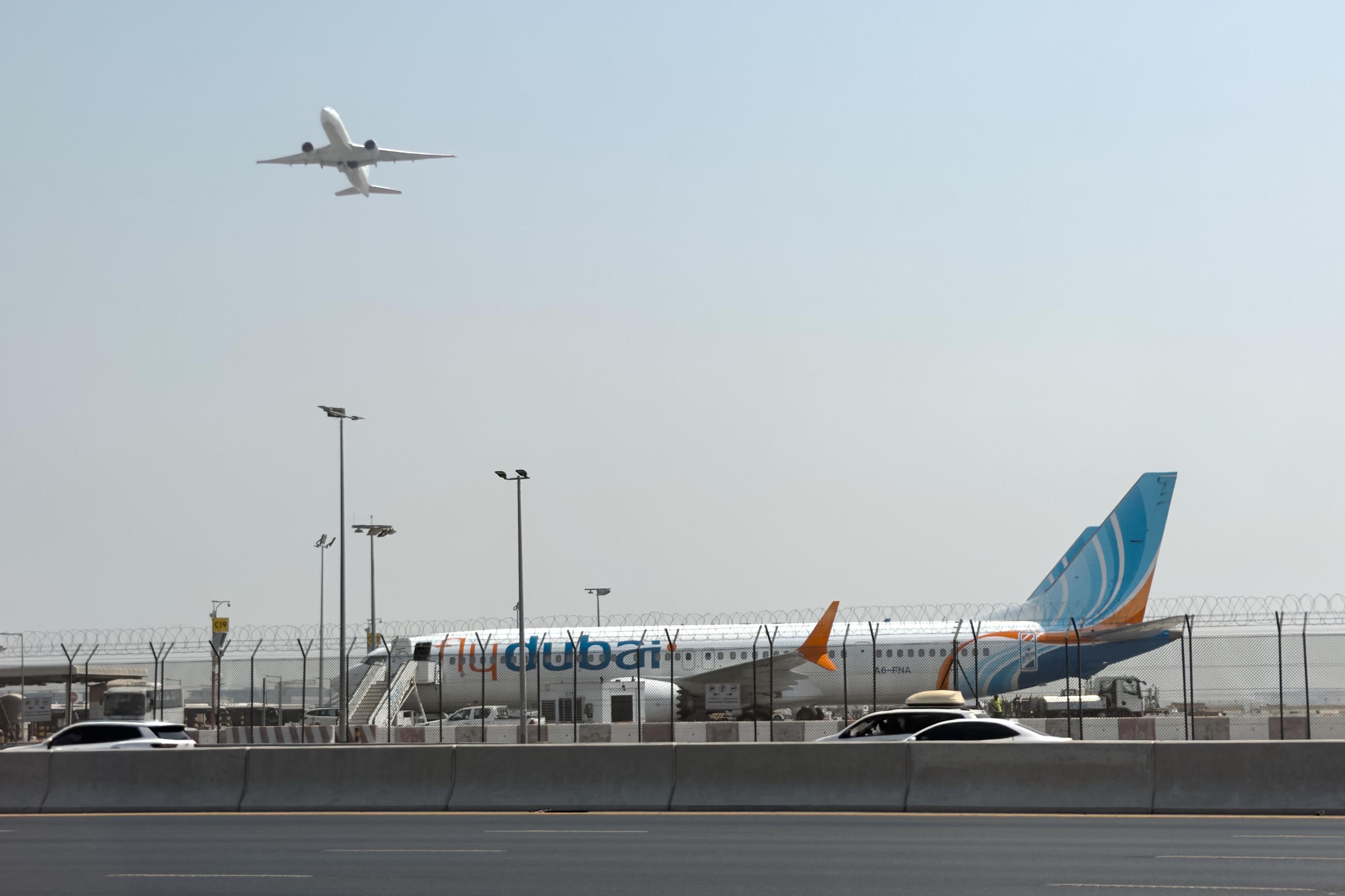 A plane takes off as a Flydubai aircraft sits on the tarmac at Dubai International Airport.
