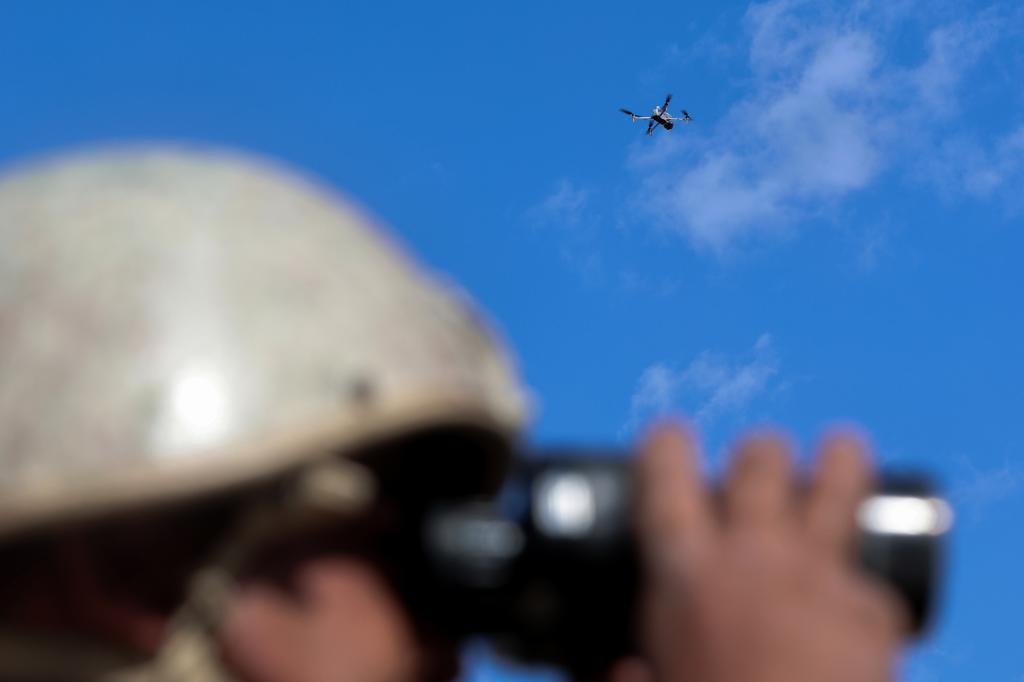 A border guard uses binoculars as a drone flies above during training exercises