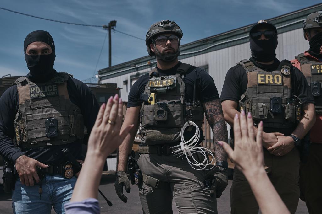 A protester holds her hands up as ICE agents guard the Delaney Hall detention center