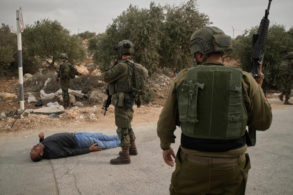 Israeli soldiers, alongside a wounded Palestinian lying on a road
