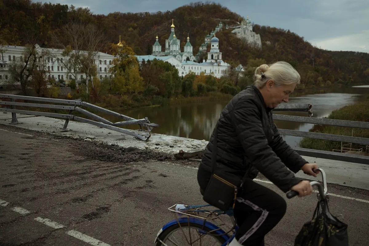 A woman crosses the Sviatogirst bridge with her bicycle.