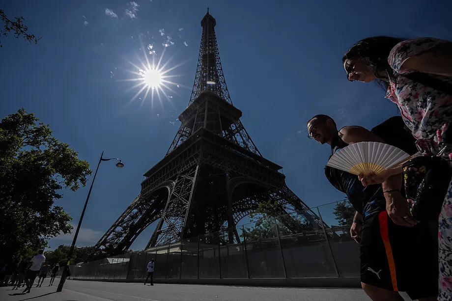 People walk with fans near the Eiffel Tower in Paris during a heatwave in July .
