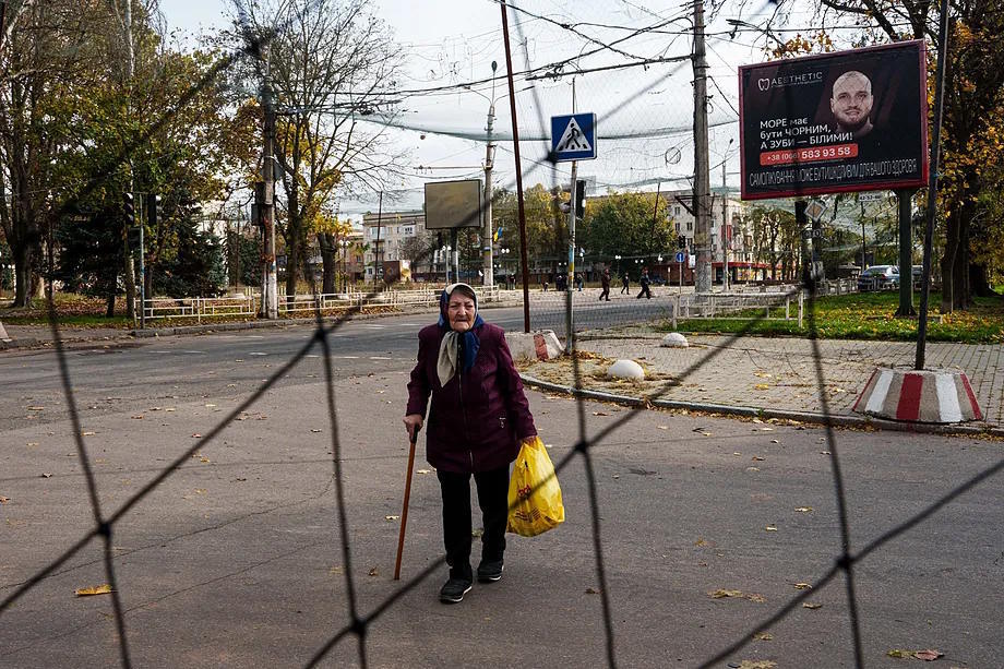 An elderly woman walks under drone nets stretched across a street during a ceasefire in the Ukrainian city of Oleshky, in Kherson.